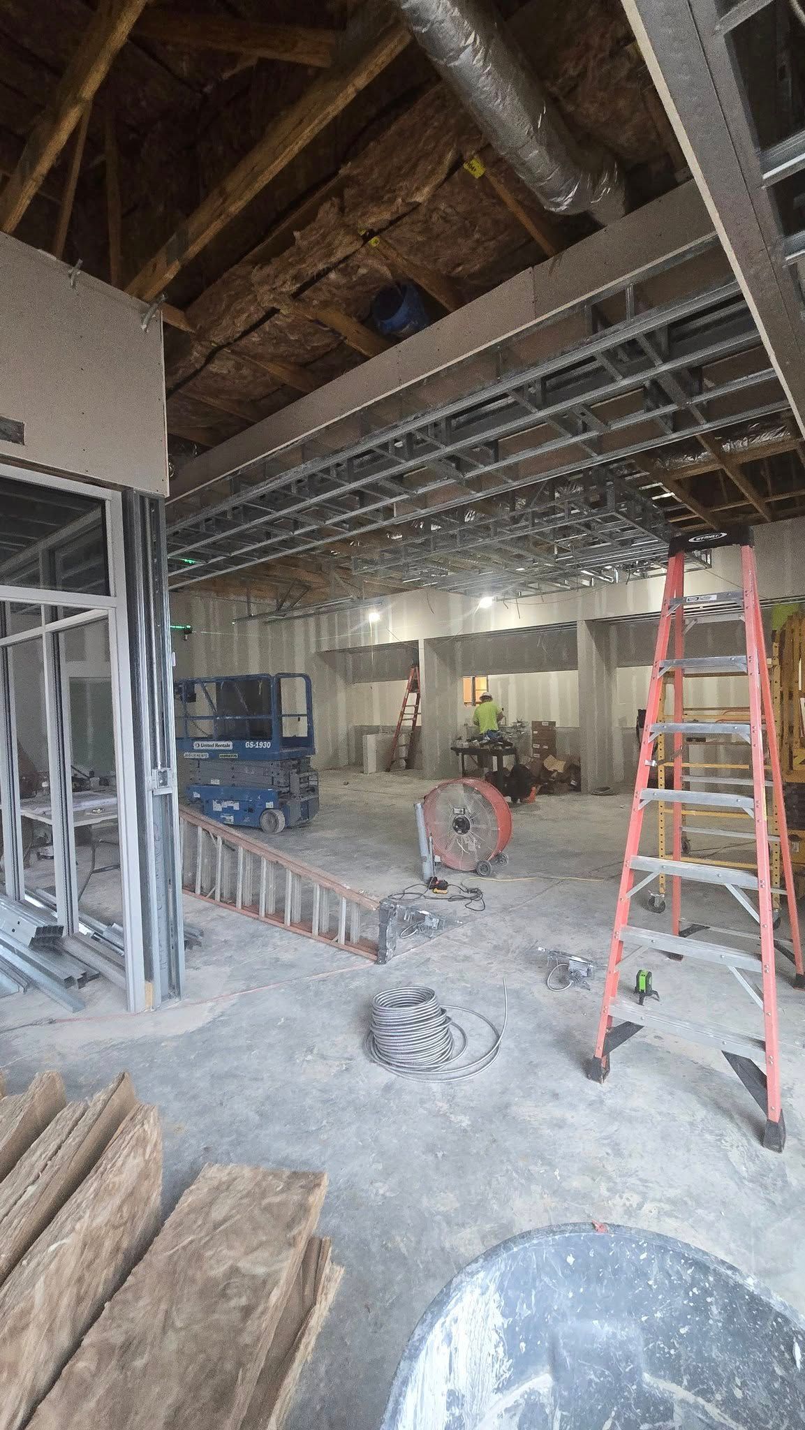Interior construction site. Metal studs, exposed ceiling, concrete floor, red ladder, and construction.