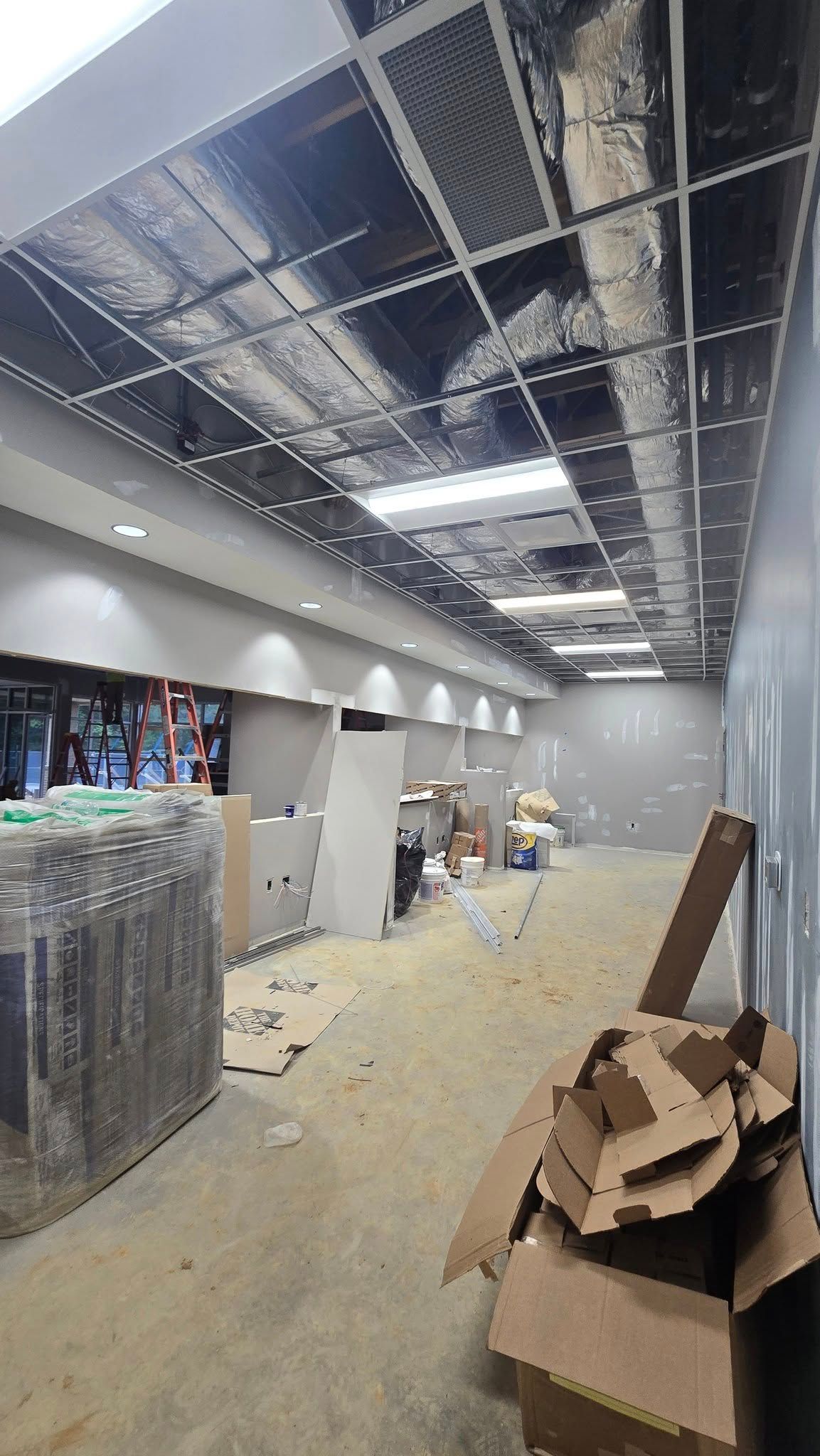 Construction site: long hallway with unfinished ceiling, debris on the floor, and materials stacked.