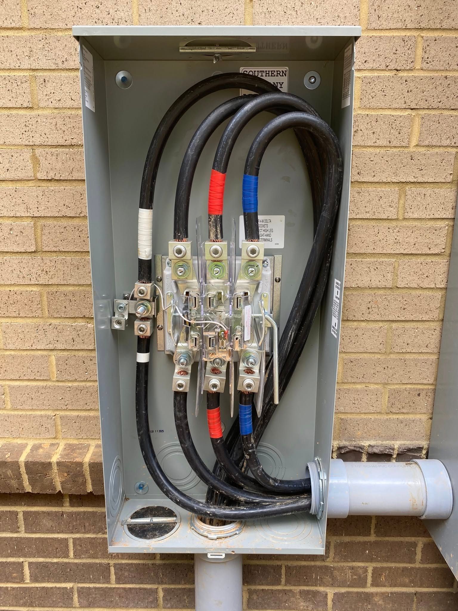 Electrical panel with black cables, red/blue taped wires, and metal components.