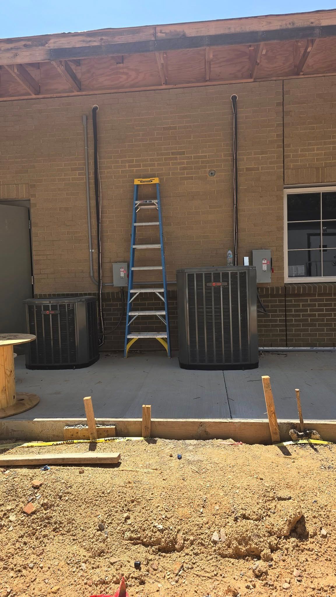 Construction site with a ladder against a brick building, two large black tanks, and electrical boxes.