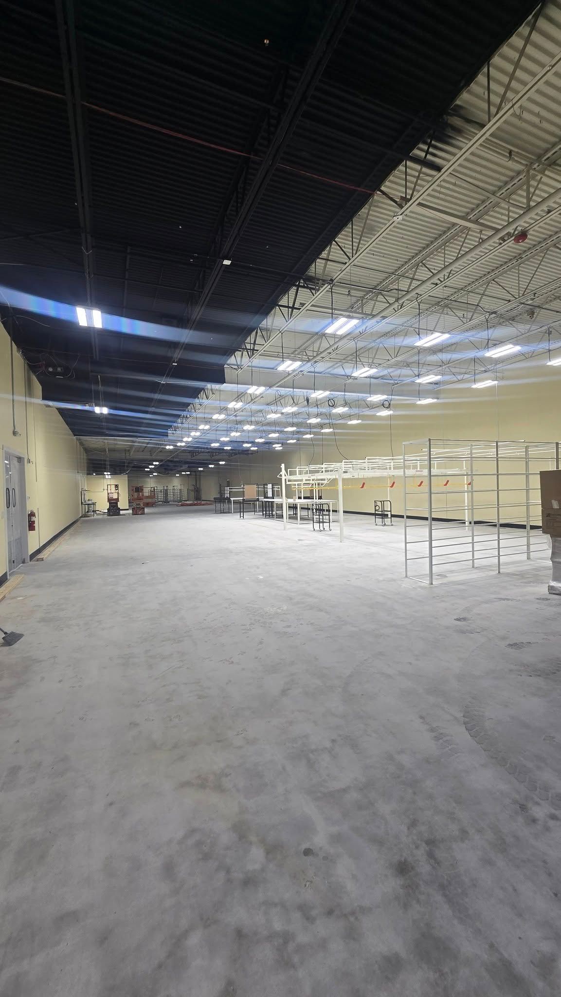Interior of a large, empty commercial space with high ceilings; black and white roof, concrete floor, and minimal fixtures.