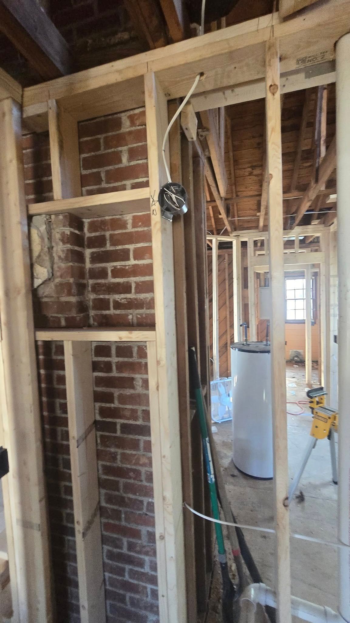 Framing and brick interior wall during home construction with electrical wiring and plumbing visible.