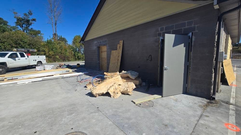 Exterior building under construction, grey block walls, debris, silver truck, blue sky.
