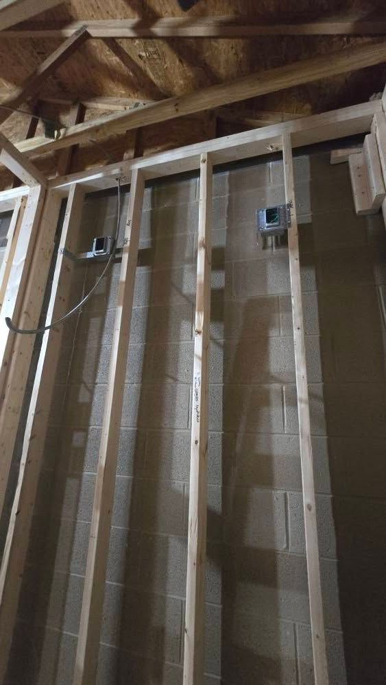 Wooden wall studs with electrical boxes, framing a concrete block wall in construction.