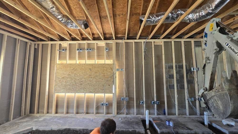 Construction site interior with exposed wooden framing, electrical boxes, and a person working on the ground.