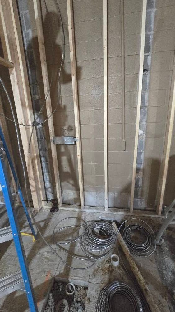 Construction site interior with exposed framing, electrical conduit, and coiled wires on the floor.
