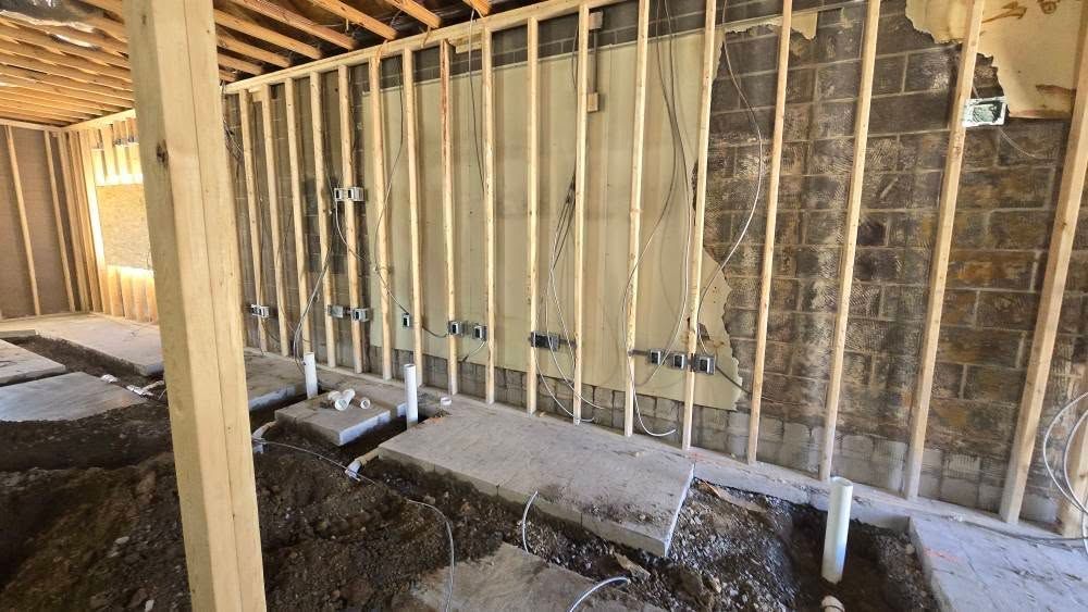 Interior of a building under construction, showing exposed framing, plumbing, and debris.