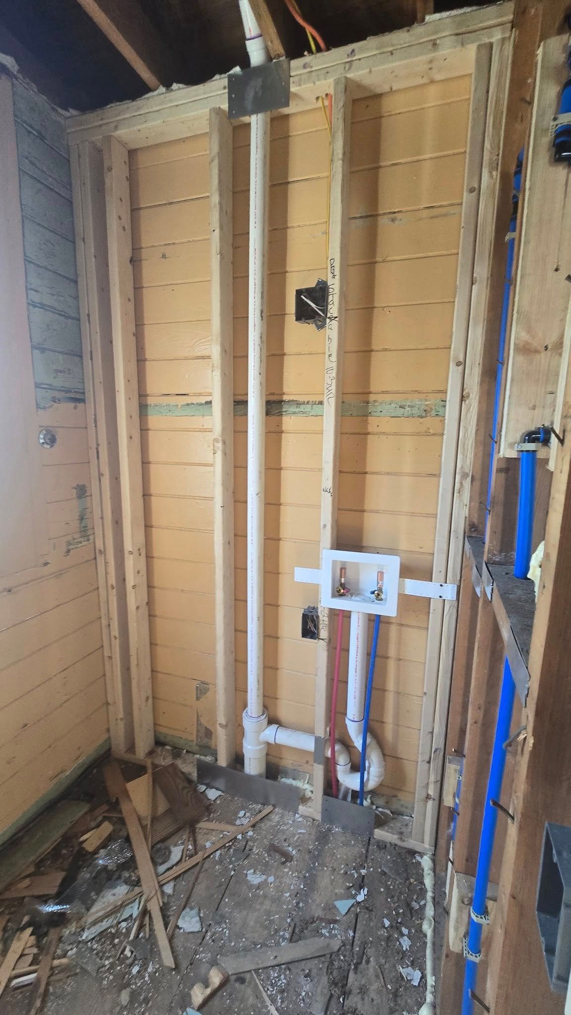Interior wall framed for bathroom renovation, showing plumbing pipes and electrical box.