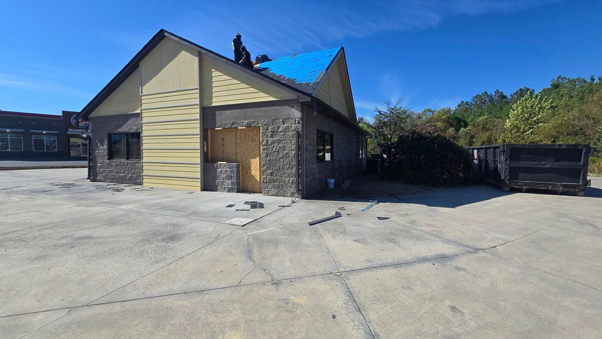 Building under renovation with exposed stone and blue roof, surrounded by debris and a dumpster.