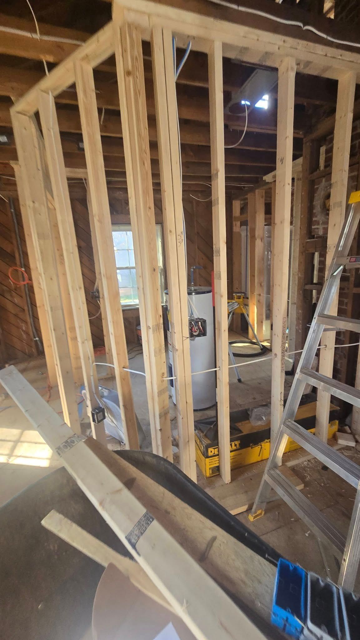 Interior framing of a room under construction with a water heater visible. A ladder leans against the right wall.