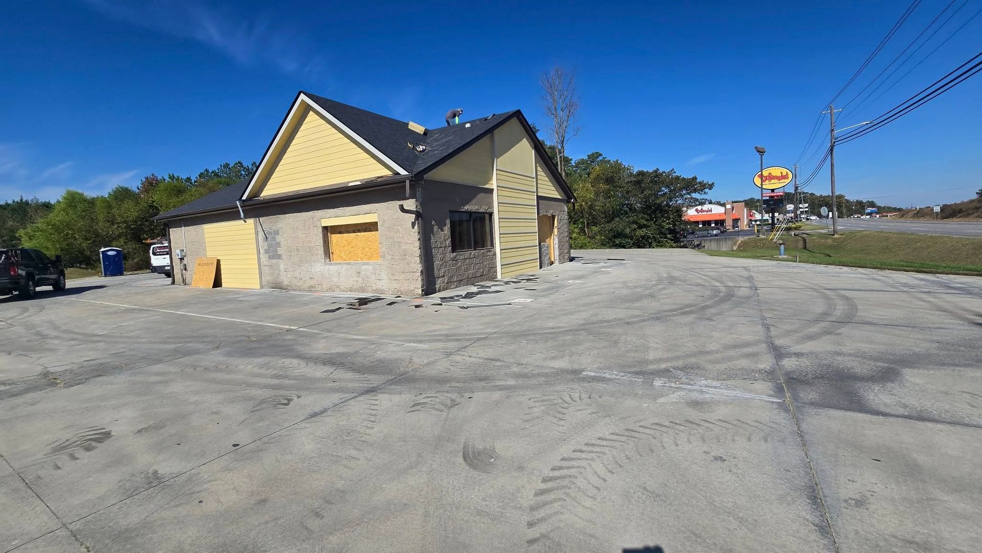 Building under construction on a concrete lot, blue sky, yellow trim, and black roof.
