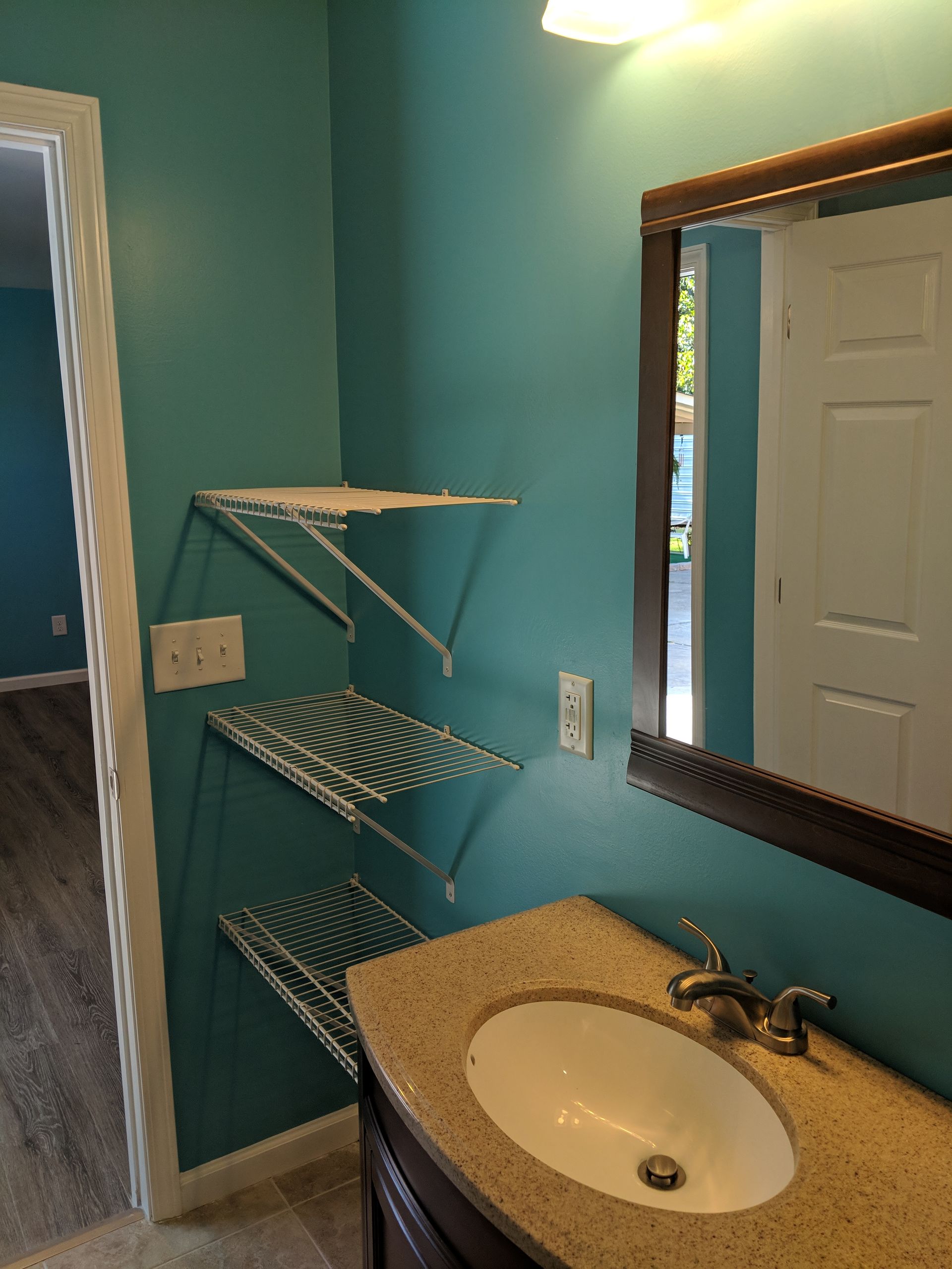 Bathroom with turquoise walls, white wire shelves, and a vanity with a sink.