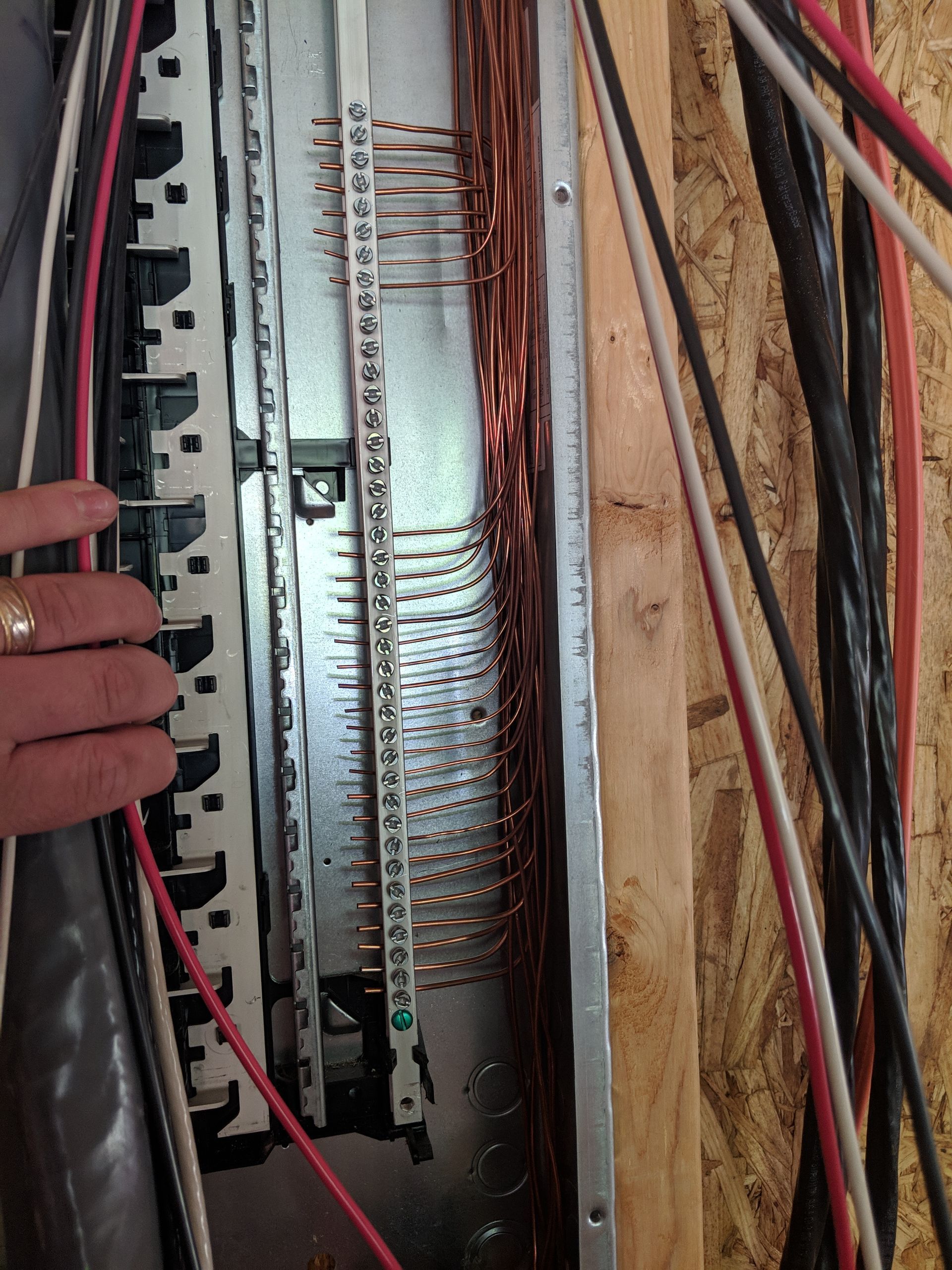 Electrical panel with copper wires, breakers, and a hand pointing.