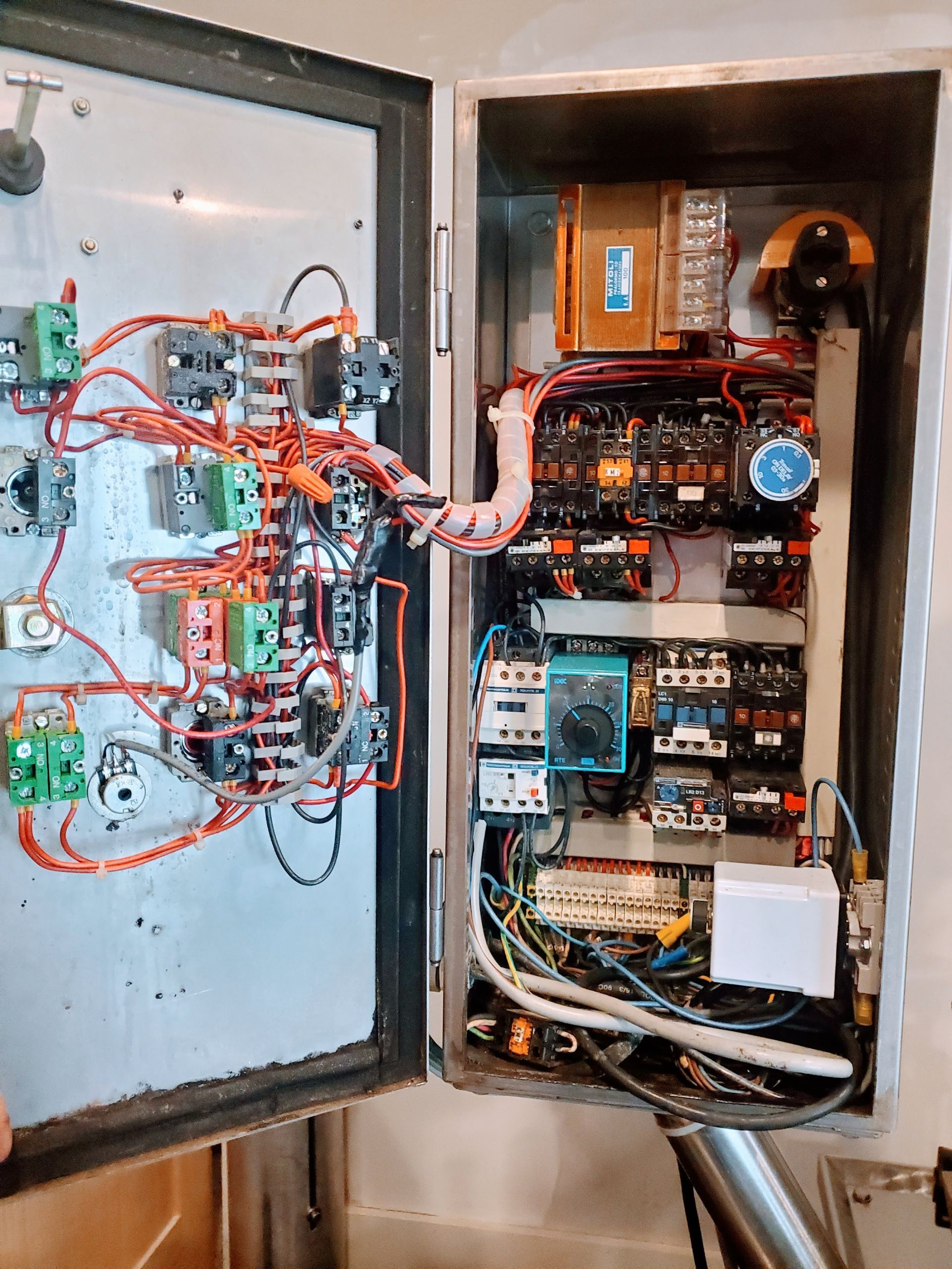 Open electrical panel with wires, relays, and components mounted on a metal surface.