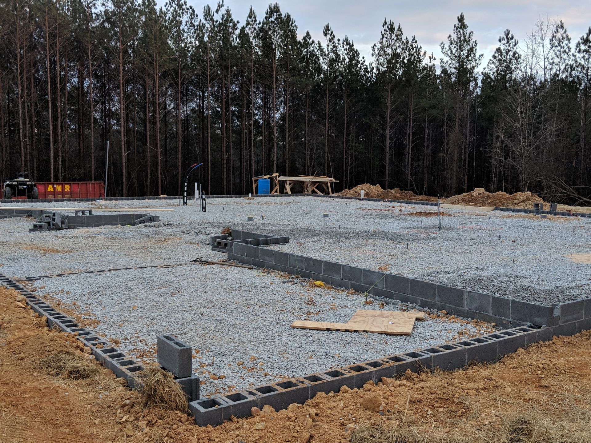 Foundation of a building under construction, grey blocks, gravel fill, trees in the background.