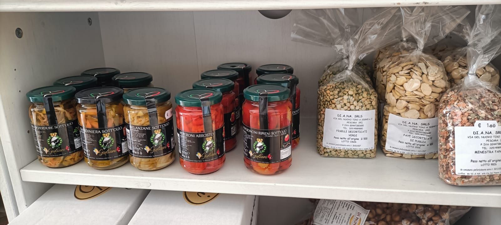 Barattoli di vetro contenenti conserve e funghi secchi, disposti su scaffali bianchi della dispensa.
