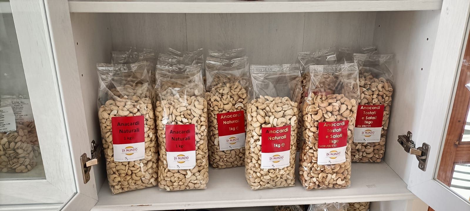 Sei barattoli trasparenti di cereali con etichette rosse esposti su uno scaffale bianco