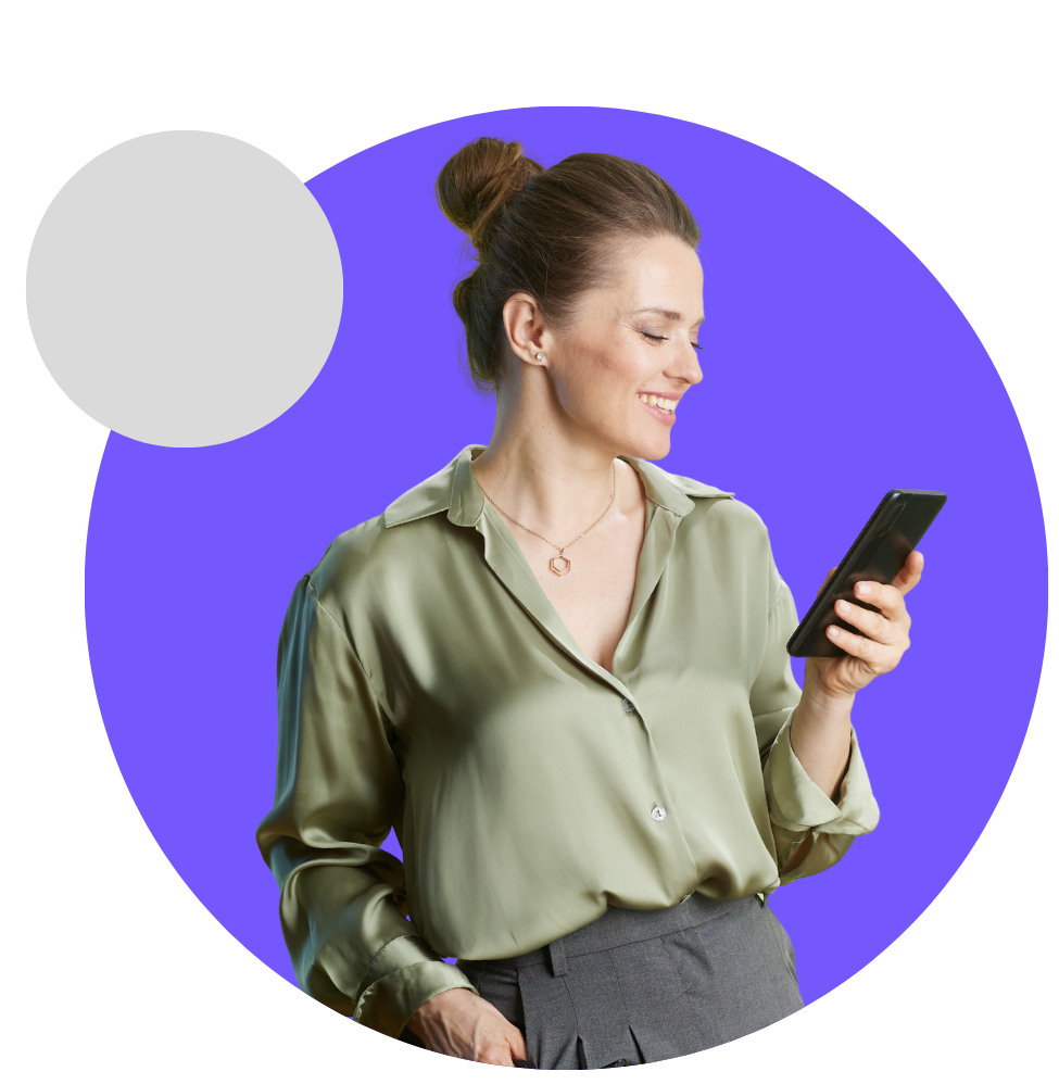 Woman smiling, looking at a smartphone, wearing a green blouse and gray pants against a purple background.