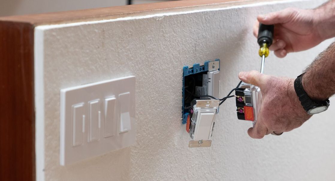 A person is installing a light switch on a wall with a screwdriver.