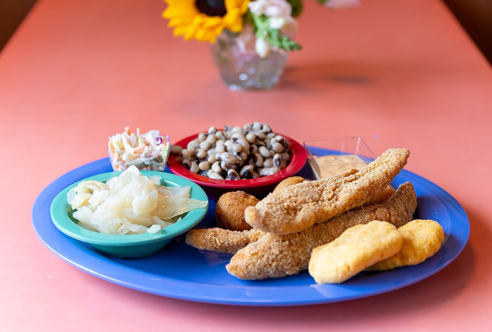 A blue plate topped with fried fish , nuggets , coleslaw and black eyed peas.