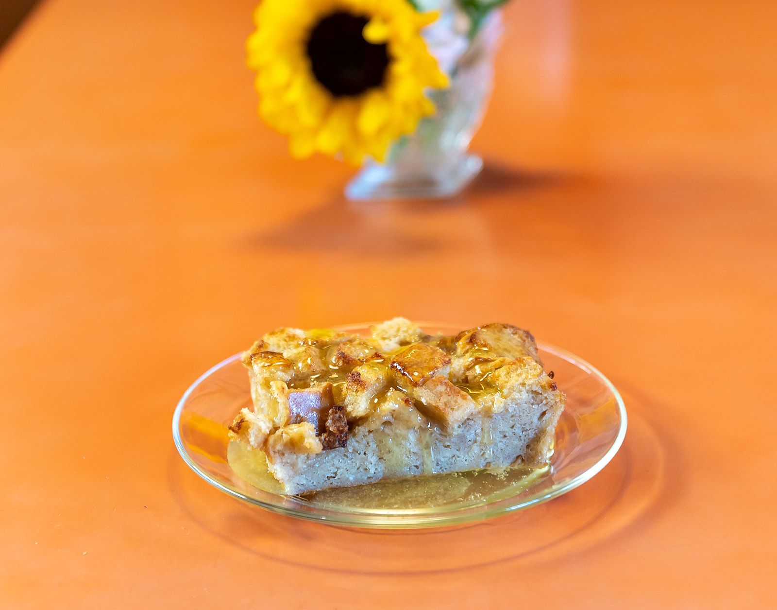 A piece of bread pudding is on a glass plate on a table.