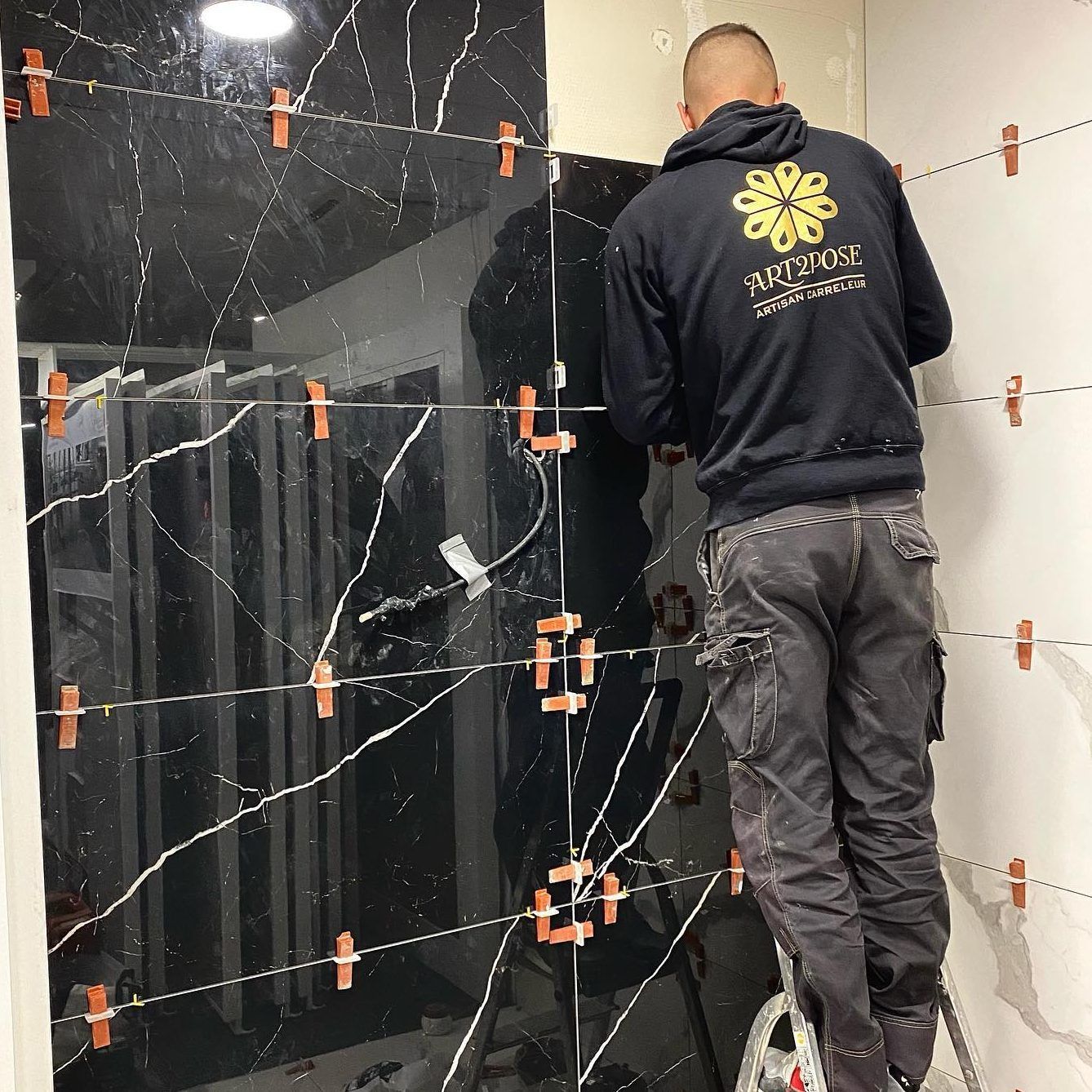 un homme se tient sur une échelle devant un mur noir.