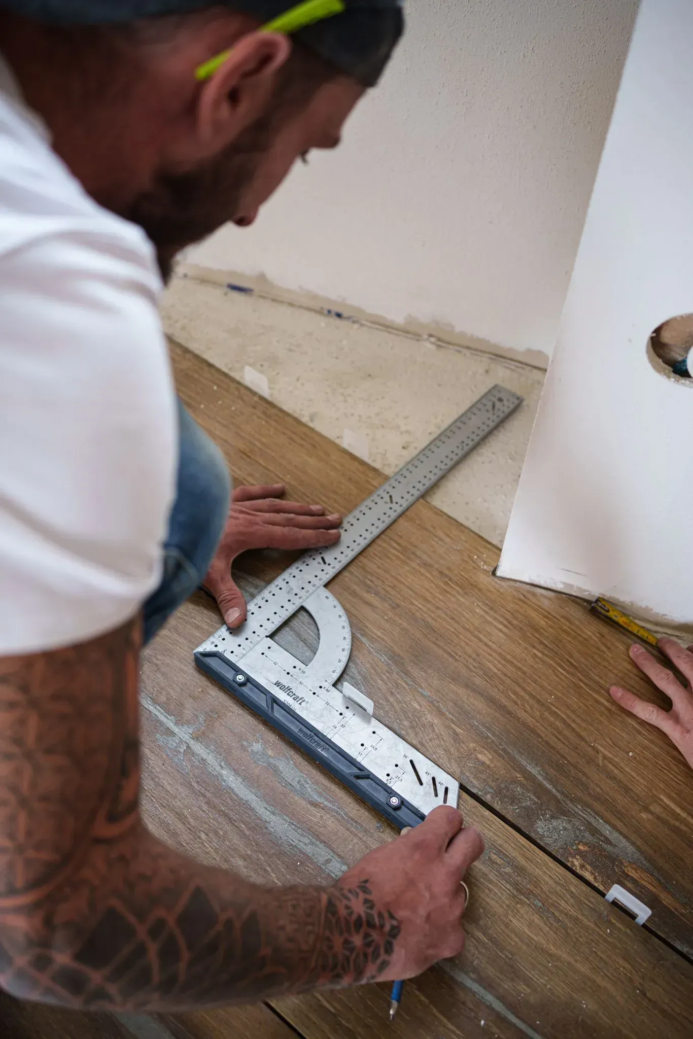 un homme mesure un parquet avec une règle.