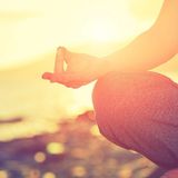 A woman is sitting in a lotus position on the beach at sunset.