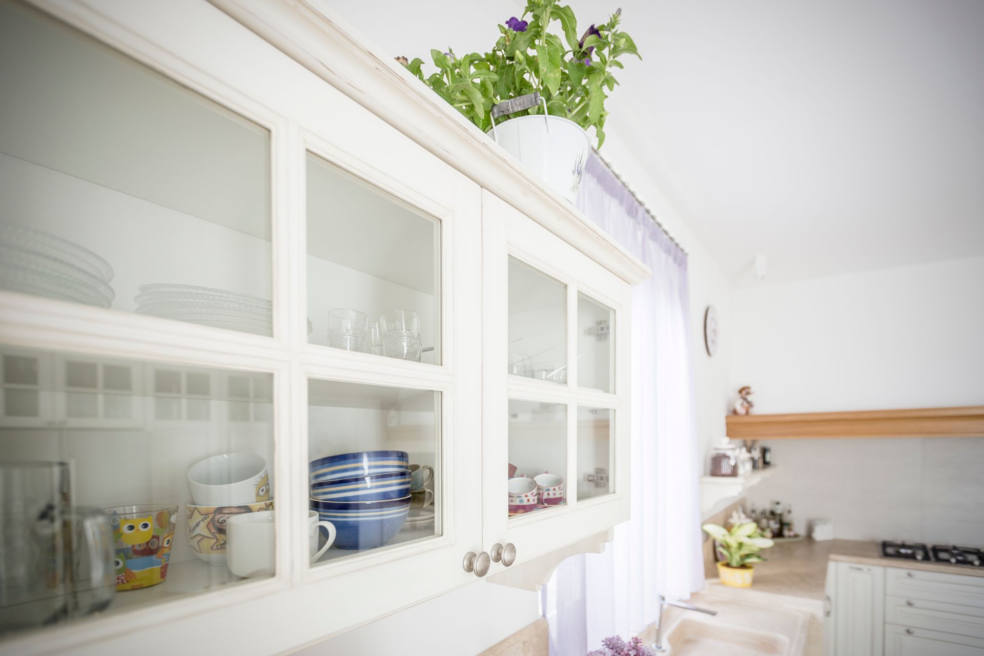 Una cucina con mobili bianchi e porte in vetro piene di piatti.