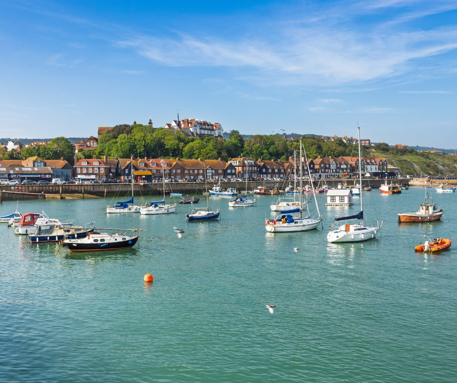 The Folkestone Harbour with the tide in and various fishing boats. In the background are the houses.
