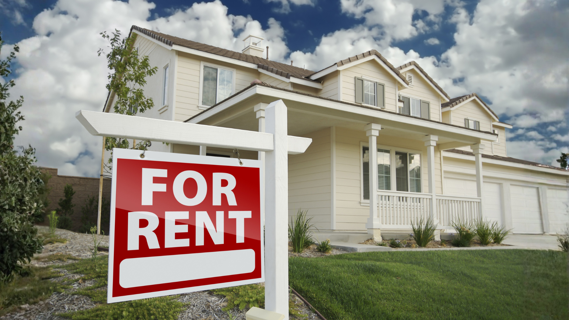 House for rent, red and white sign in front of two-story beige house with green lawn.