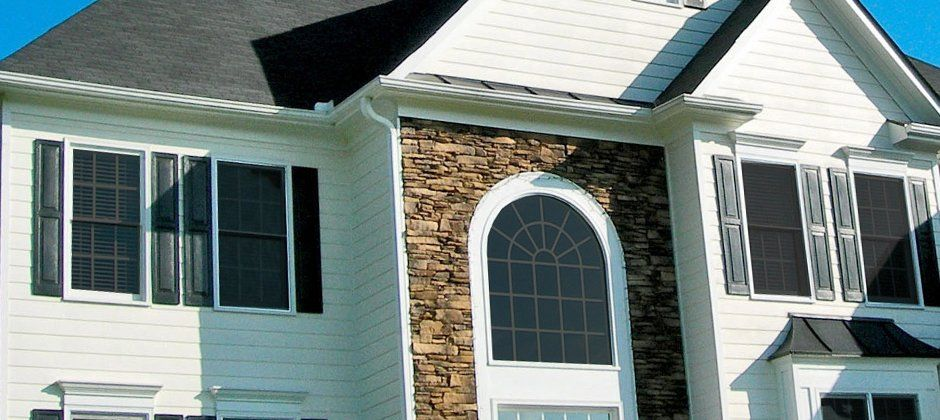 A large white house with black shutters and a stone wall