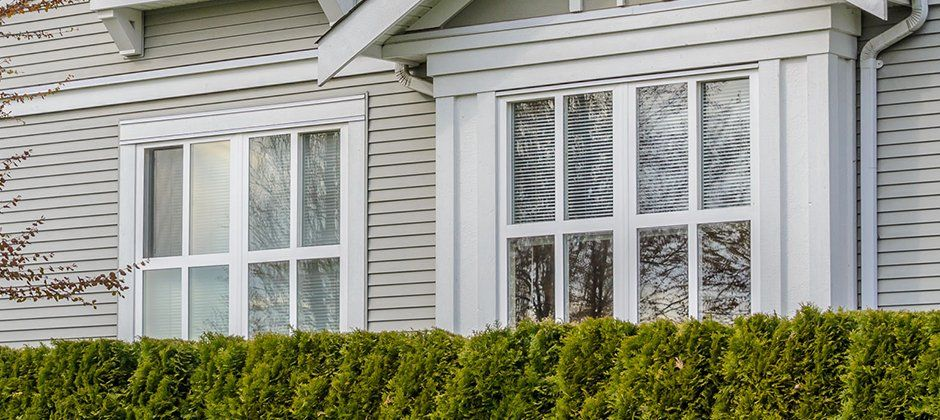 A white house with a large window and a hedge in front of it.