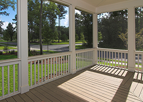 A screened in porch with a wooden deck and a white railing.