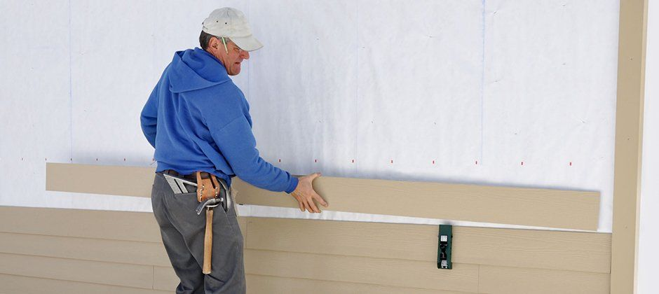 A man is measuring a piece of siding on a wall.