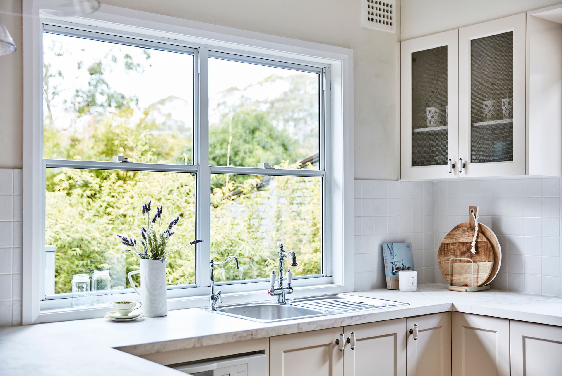 A kitchen with white cabinets , a sink , and a large window.