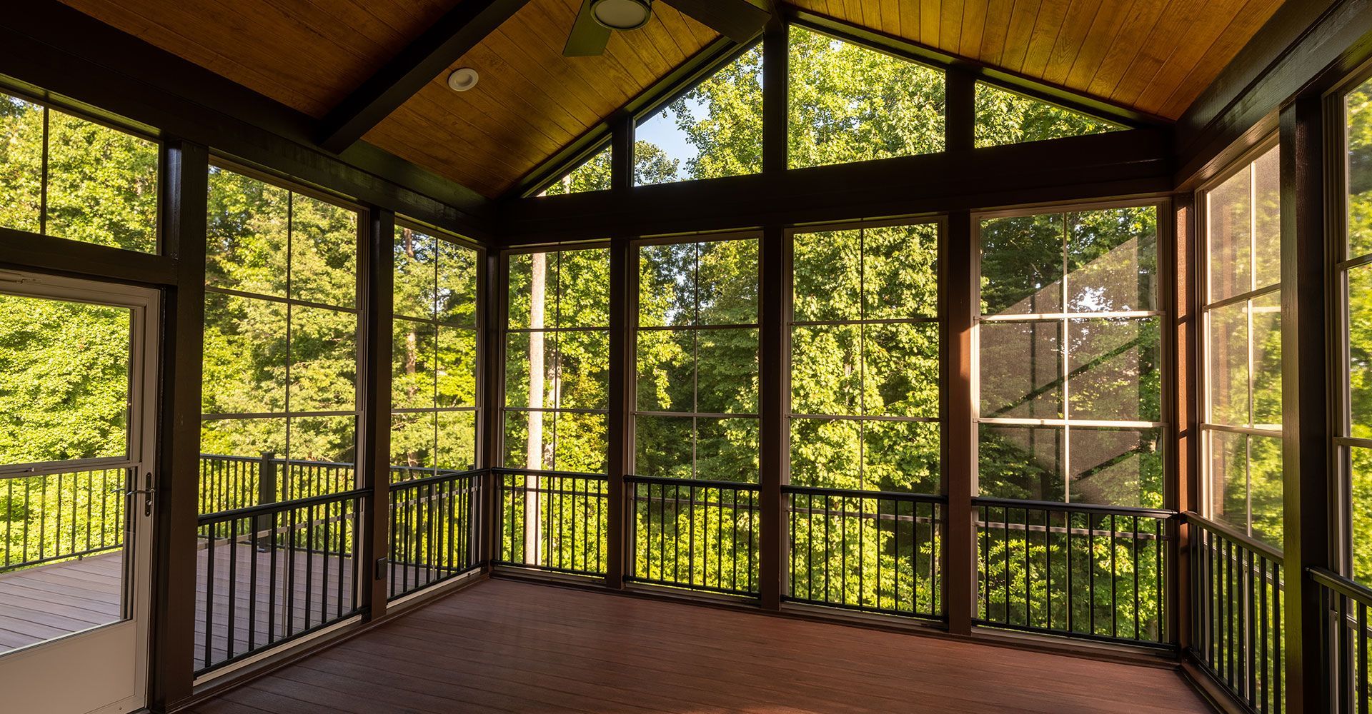 A screened in porch with lots of windows and trees in the background