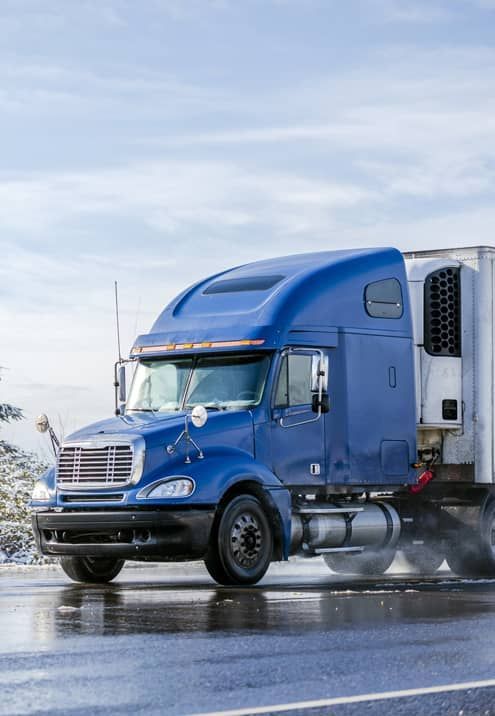 A blue semi truck is driving down a wet road.