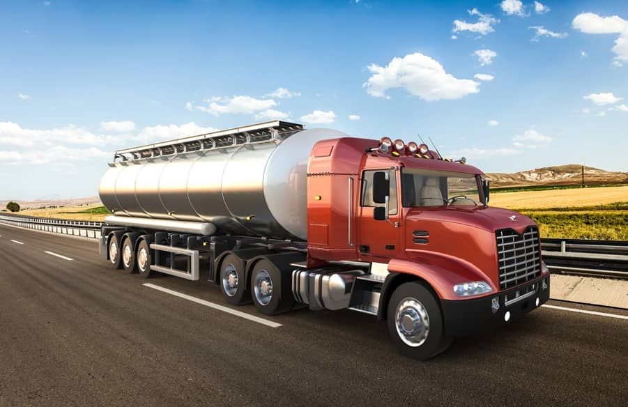 A red semi truck with a tanker trailer is driving down a highway.