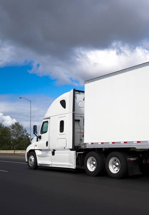 A white semi truck is driving down a highway.