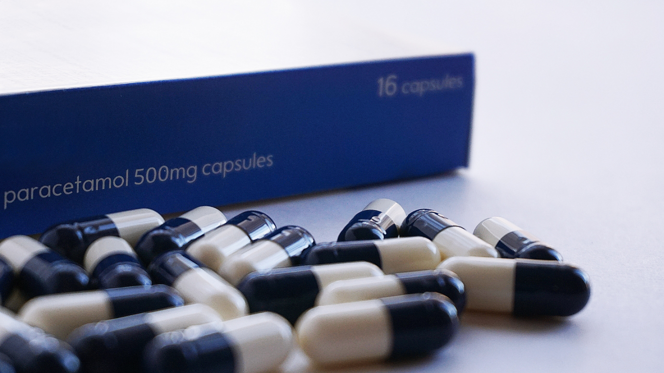 A blue box of 500mg paracetamol capsules with a pile of blue and white capsules in the foreground.