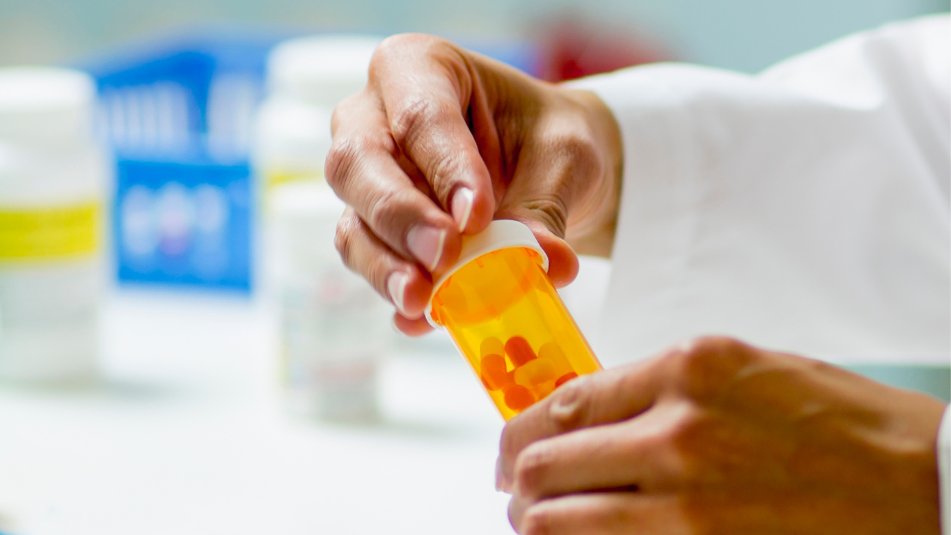 A professional in a white coat opening a small, orange prescription pill bottle.