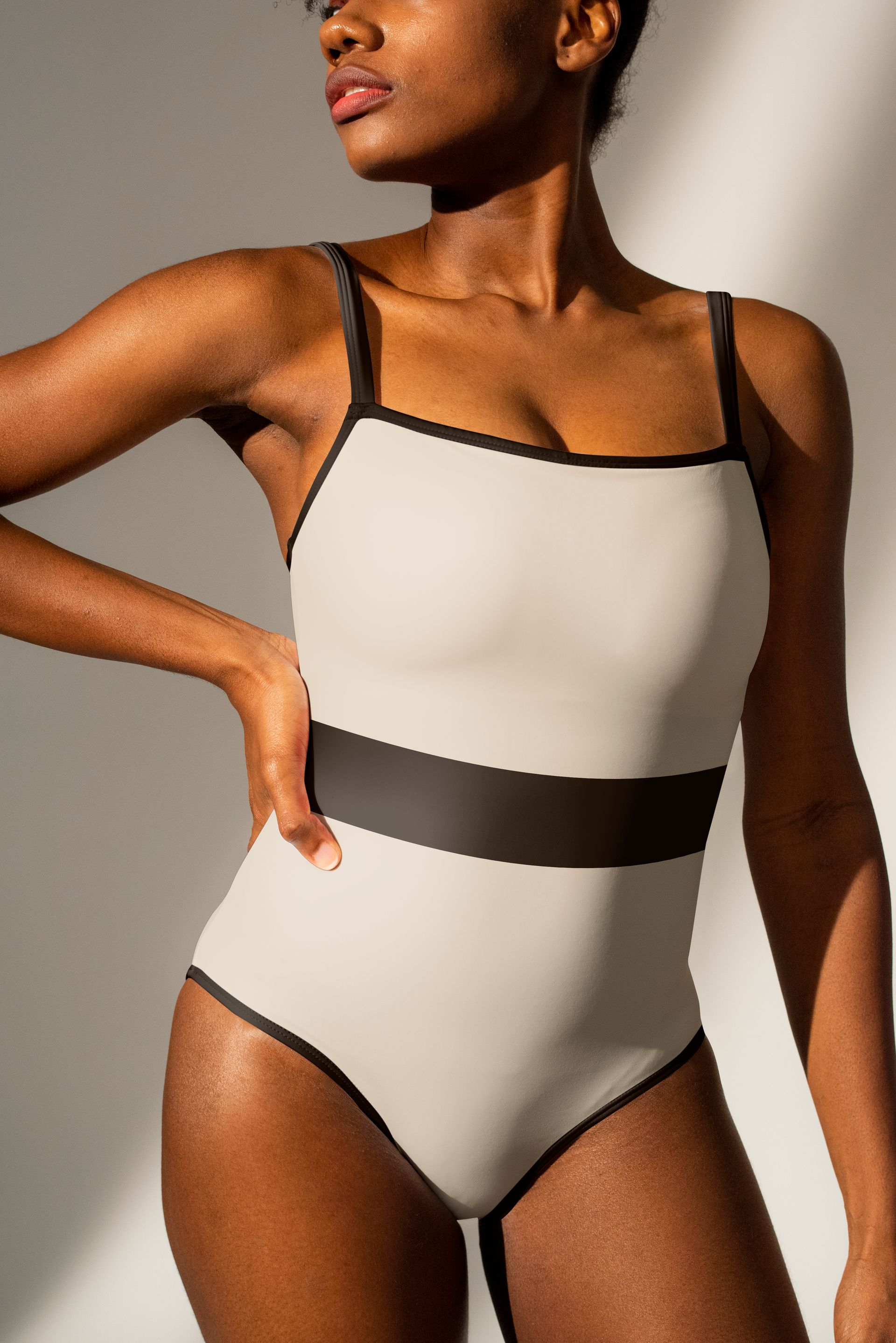A woman in a white swimsuit is standing in front of a white wall.