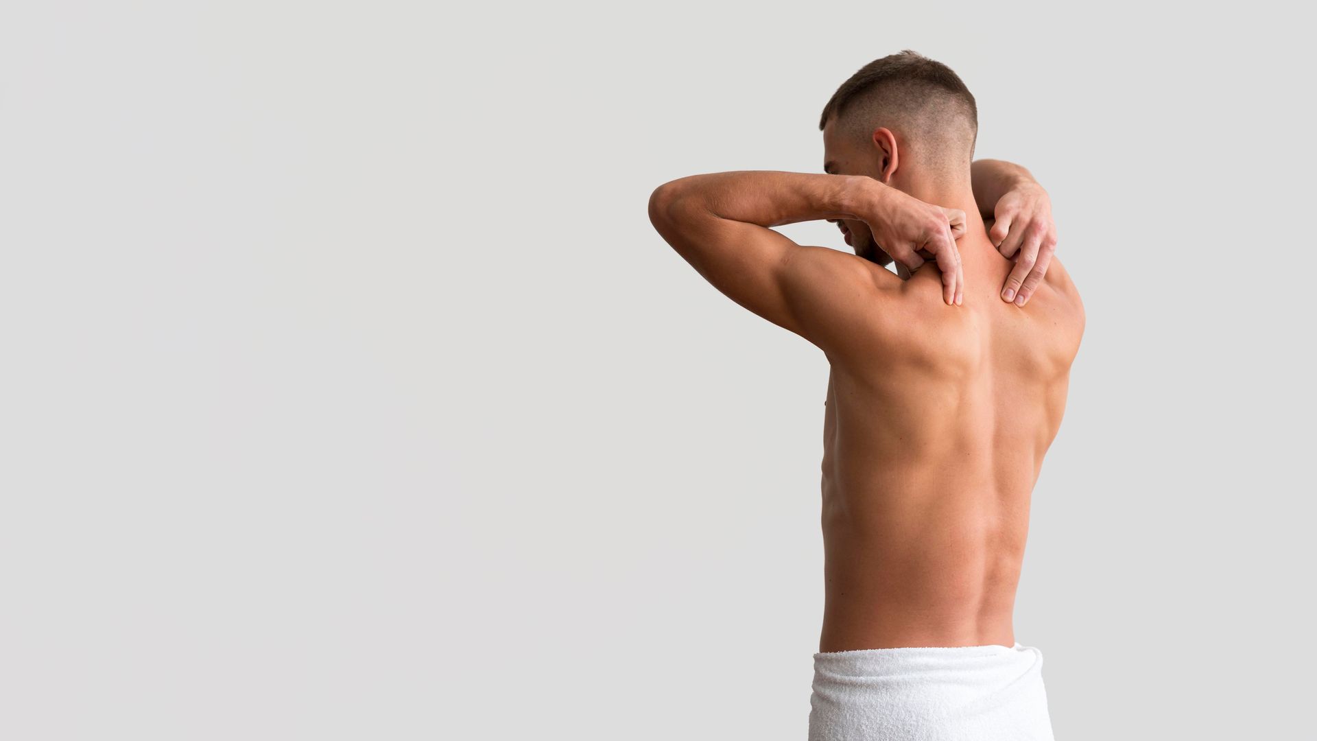 a shirtless man with a towel around his waist is holding his neck .