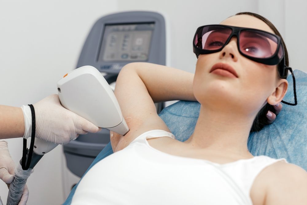 Woman receiving laser hair removal on her underarm; medical setting, wearing protective glasses.