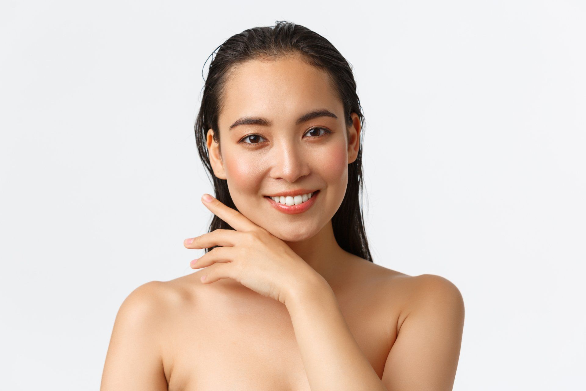 A woman without a shirt is smiling and touching her face.