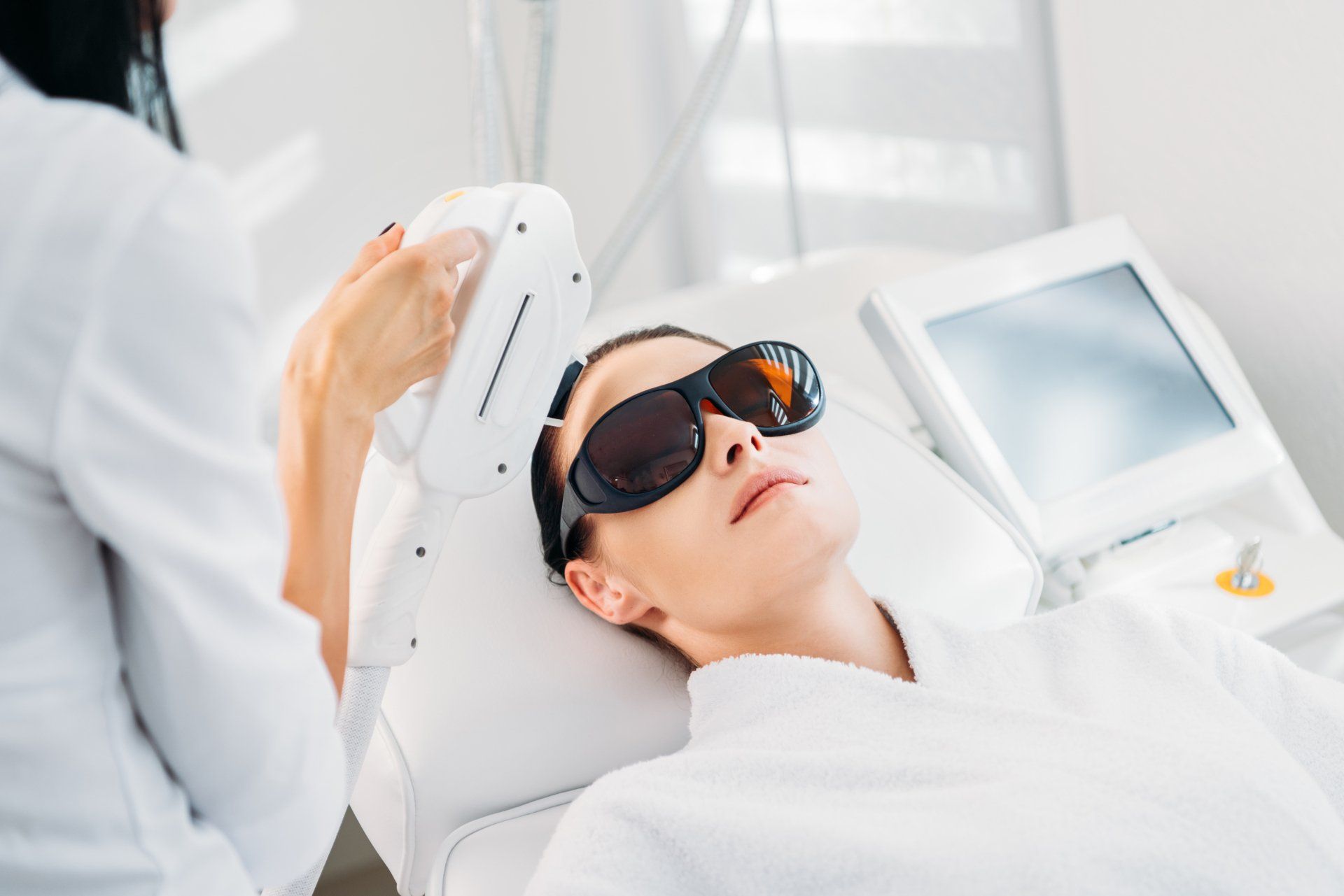 A woman wearing sunglasses is getting a laser treatment on her face.