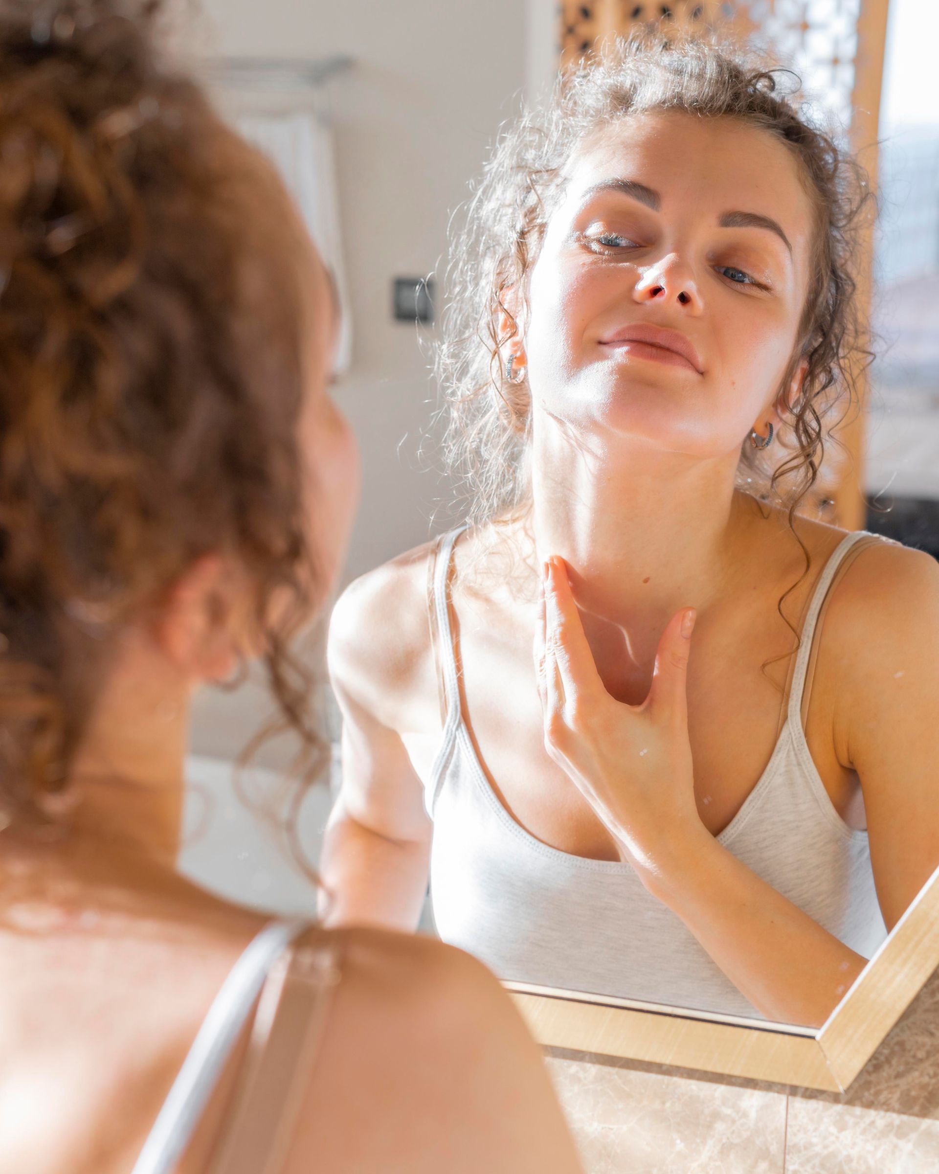 A woman is looking at her reflection in a bathroom mirror.