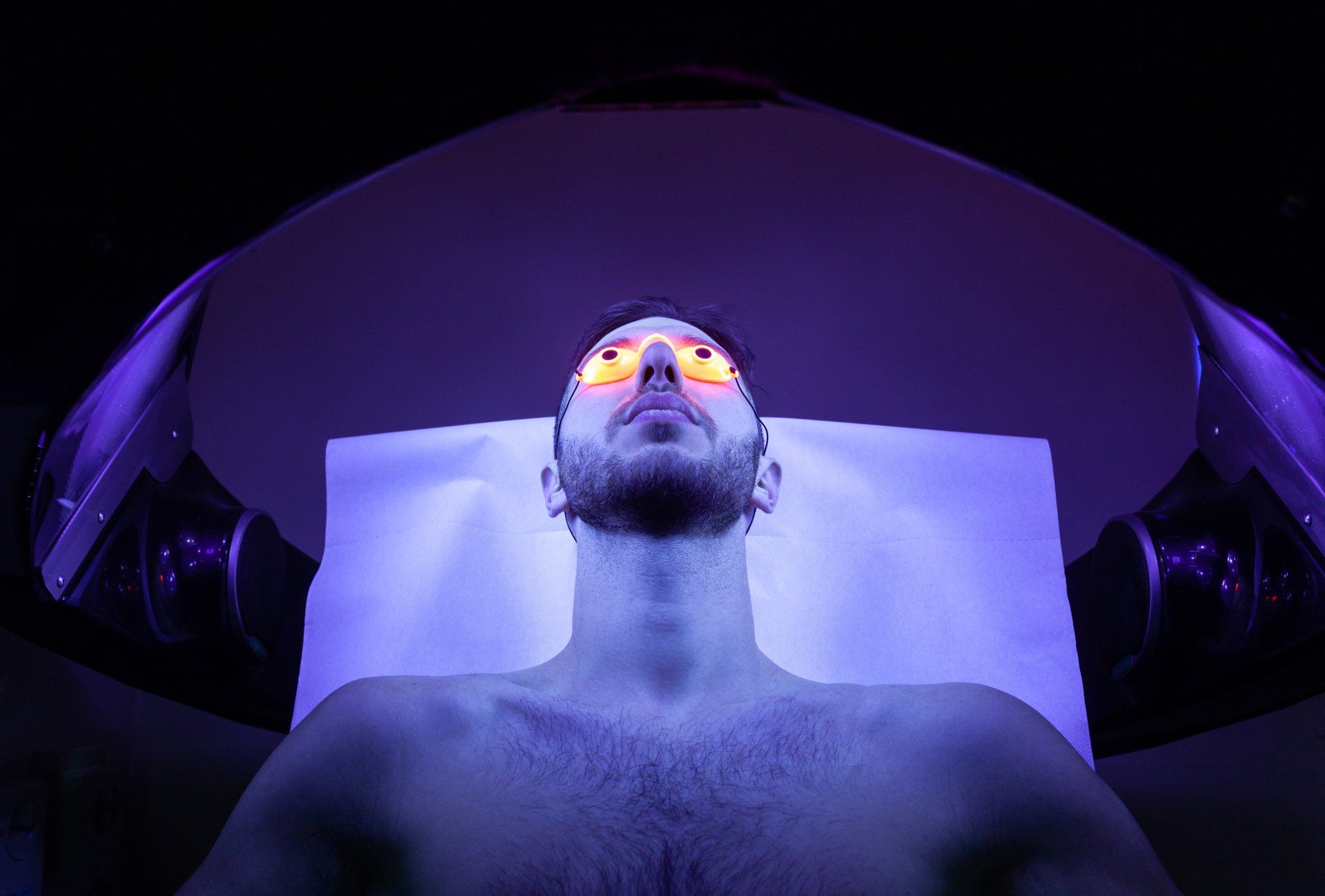 A man is laying on a bed under a purple light.