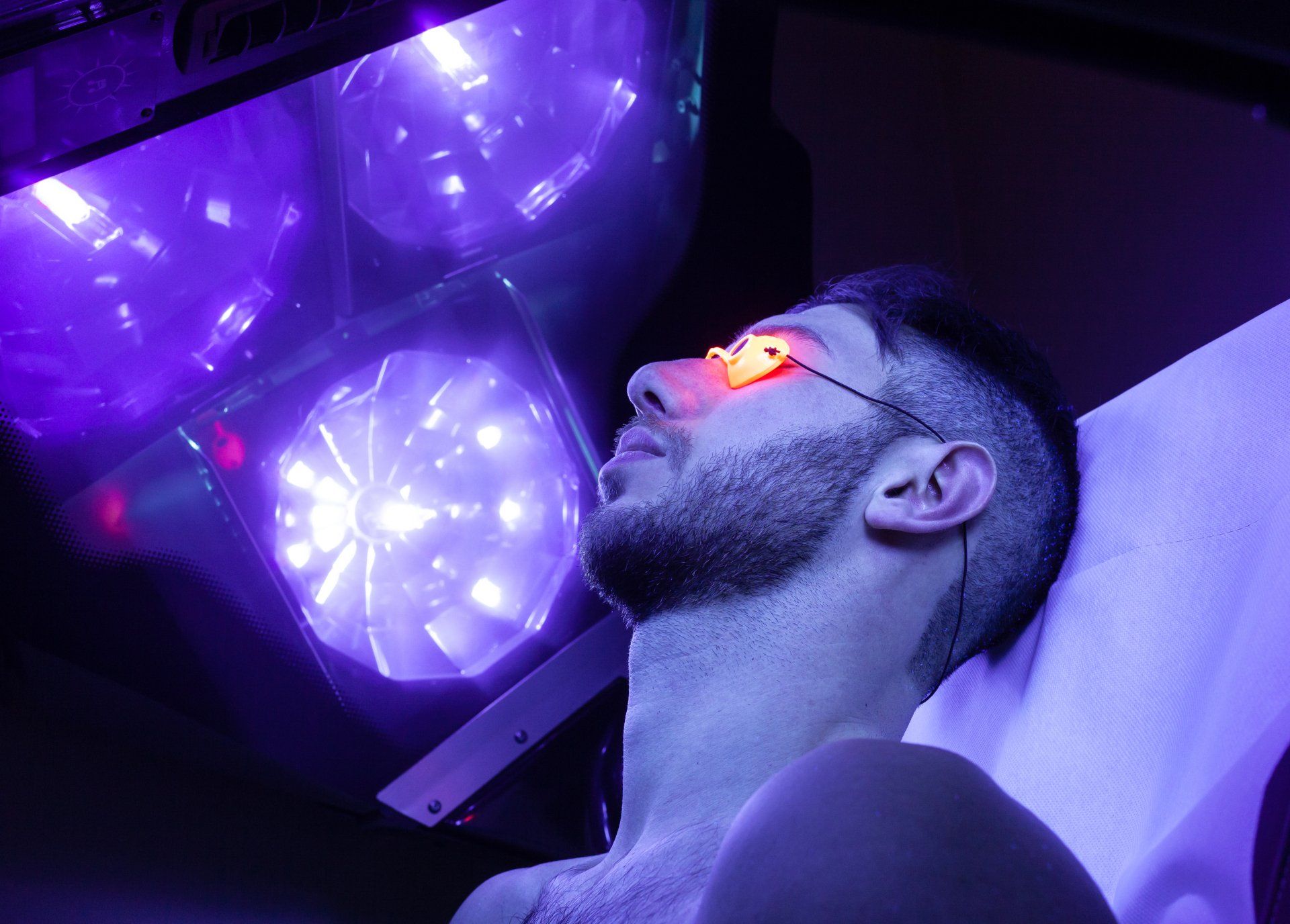 A man is laying in a bed with purple lights on his face.